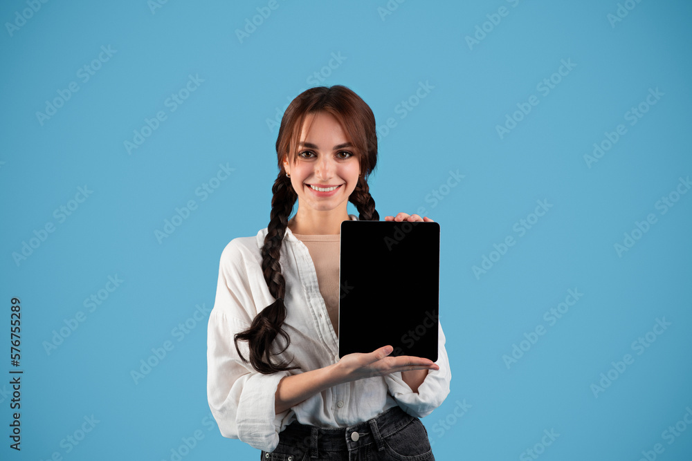 Obraz premium Smiling teen european girl student with pigtails show tablet with blank screen