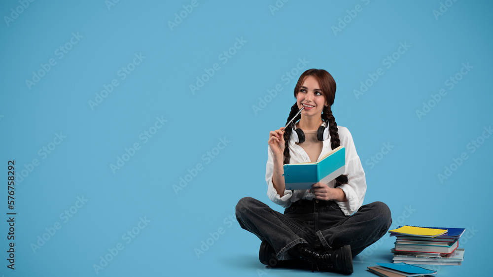Glad pensive teen european girl with pigtails plans day, think with notebook, looks at copy space