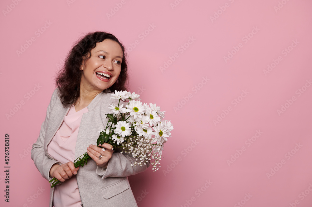 Attractive mature woman smiling a beautiful toothy smile, looking aside at copy ad space, posing with a cute bouquet of flowers for International Women's Day, isolated pink color background. 8 March Attractive mature woman smiling a beautiful toothy smile, looking aside at copy ad space, posing with a cute bouquet of flowers for International Women's Day, isolated pink color background. 8 March