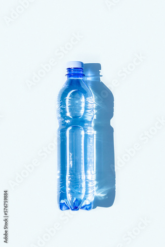 Bottled water. A bottle of mineral water with hard shadows on blue background. Flat lay Top view Copy space