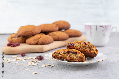 Blurred image of oatmeal cookies, oatmeal and dried cranberries and a cup of tea in the background.