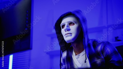 hacker wearing a white mask is using a computer to steal confidential information.Concepts: computer crime, burglary, business security on computer networks
 photo