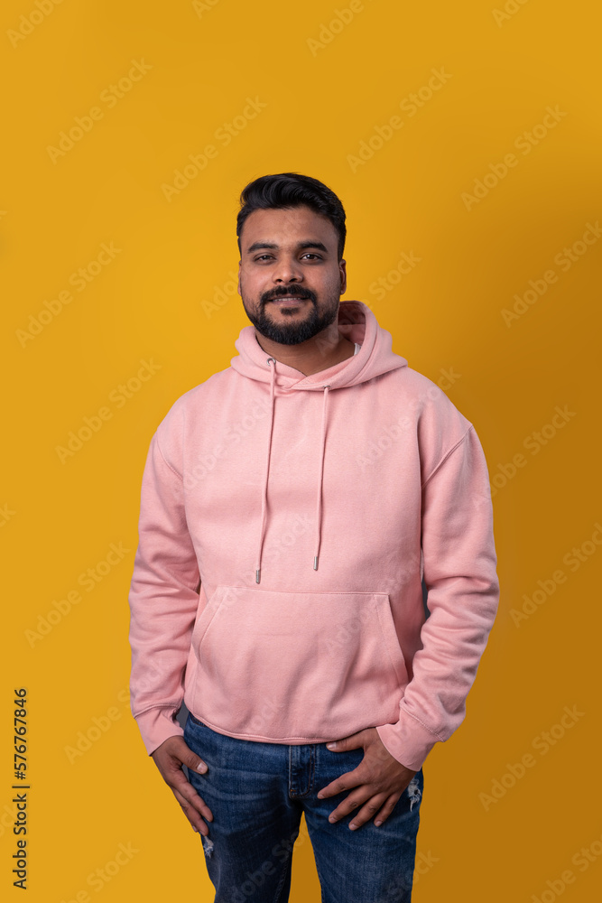Men in pink clothes. Smiling handsome Pakistani guy looking at camera. Casual pink hoodie hands in pockets. Attractive smile. Yellow background. Positive mood. Template clothes Men in pink clothes. Smiling handsome Pakistani guy looking at camera. Casual pink hoodie hands in pockets. Attractive smile. Yellow background. Positive mood. Template clothes