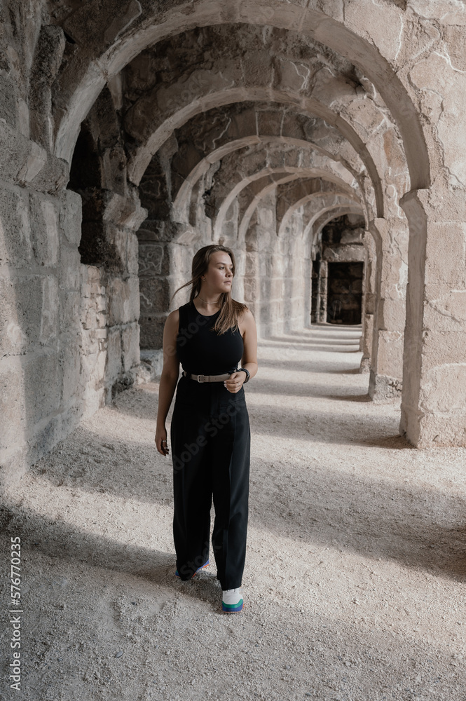 a girl in black clothes walks through antique arches