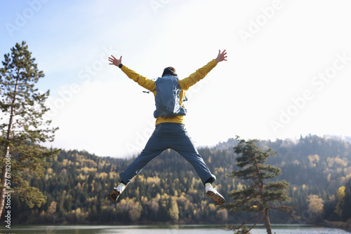 Man tourist with open arms jumping, lake and mountains on background