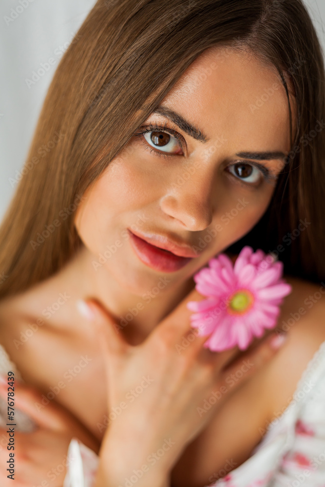 Portrait of young beautiful long-haired brown-eyed woman with pink gerbera on white background. Spring. Holidays. Mothers Day. Portrait of young beautiful long-haired brown-eyed woman with pink gerbera on white background. Spring. Holidays. Mothers Day.