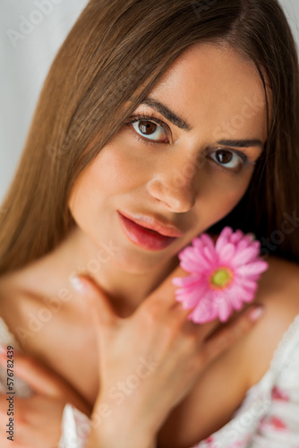Portrait of young beautiful long-haired brown-eyed woman with pink gerbera on white background. Spring. Holidays. Mothers Day.