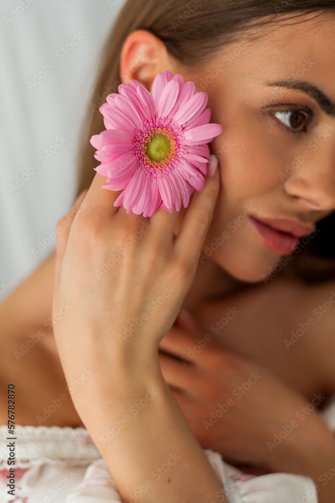 Portrait of young beautiful long-haired brown-eyed woman with pink gerbera on white background. Spring. Holidays. Mothers Day. Portrait of young beautiful long-haired brown-eyed woman with pink gerbera on white background. Spring. Holidays. Mothers Day.