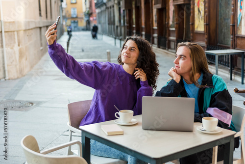 Friends taking selfies with a mobile phone while sitting at an outdoor cafe.