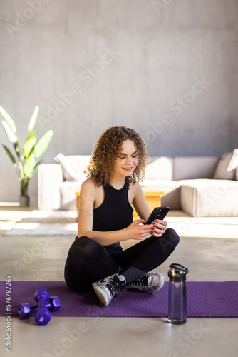 Beautiful woman looking at smartphone, listening music and relaxing after training