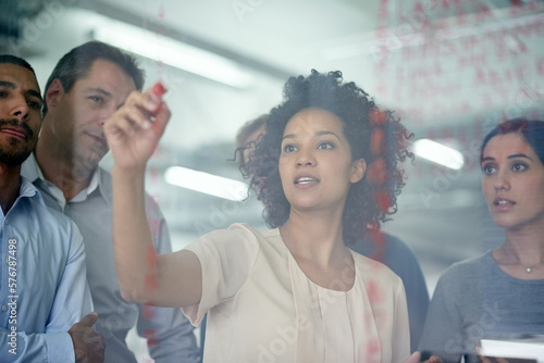 Shes got them hanging on her every word. Shot of a group of creative businesspeople plotting out details on a glass wall.