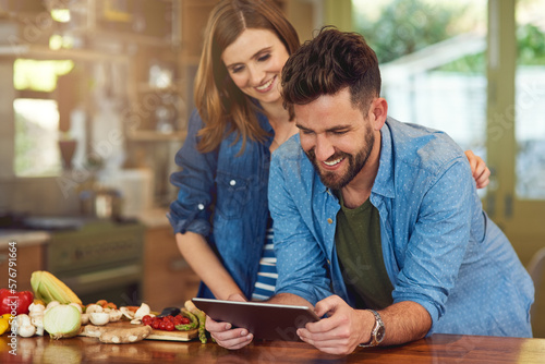 Downloading a healthy meal plan to try as a couple. Shot of a happy young couple using a digital tablet while preparing a healthy meal together at home.