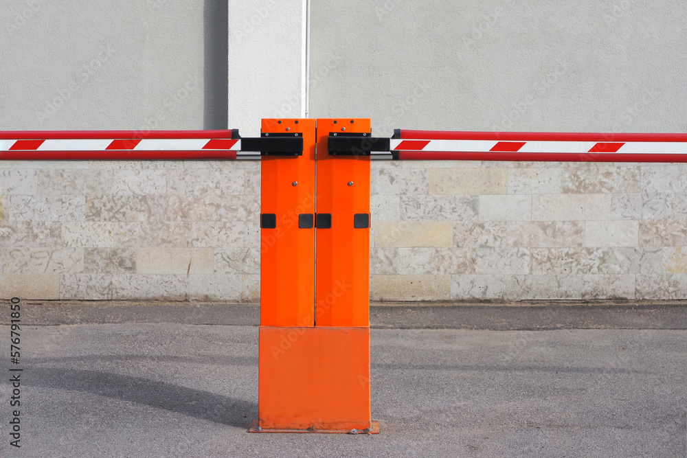 a closed red road barrier on an asphalt pre-house parking lot against the background of a gray building on a summer evening. pre-house car parking. limited parking. a closed red road barrier on an asphalt pre-house parking lot against the background of a gray building on a summer evening. pre-house car parking. limited parking.