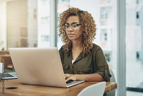 Shes one detail oriented worker. Shot of a young businesswoman using a laptop at her desk in a modern office.