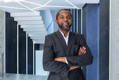 Portrait of successful african american boss, businessman in business suit smiling and looking at camera with crossed arms inside office, man satisfied with work and achievements.