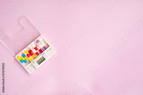 Pill box daily take a medicine, with colorful of pills, tablets, and capsules. Drugs use for treatment and cure the disease on pink background. Medicine concept. 