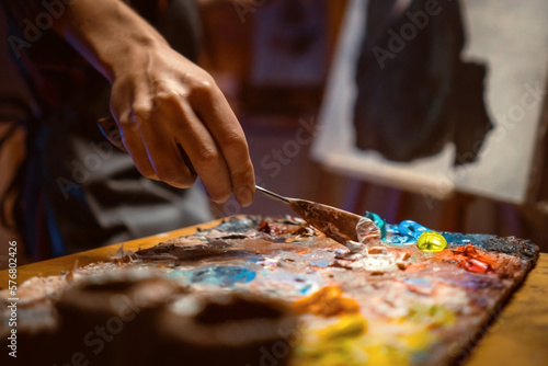 .Female artist Working on oil painting. In her hands are brushes and a palette. She paints a picture in the mysterious atmosphere of her studio. © Zhanna