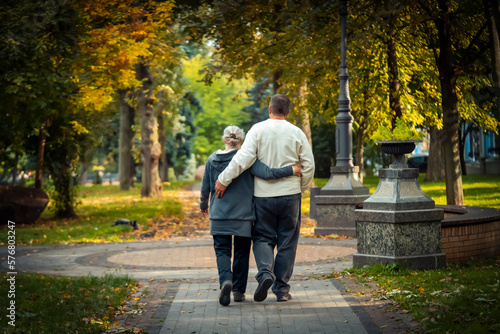 An elderly couple, man and woman walk in the autumn park. © Zhanna