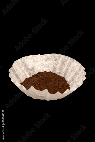 Coffee grounds in a white coffee filter on black background.