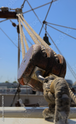 Macro of a wooden ship block with lines and ropes at a sailing ship with a blue sky in the background.