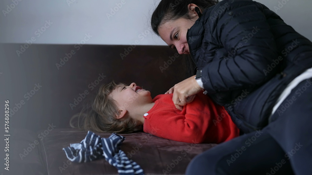 Mother tickling little boy son on home couch. Candid authentic real life mom playing with child indoors Mother tickling little boy son on home couch. Candid authentic real life mom playing with child indoors