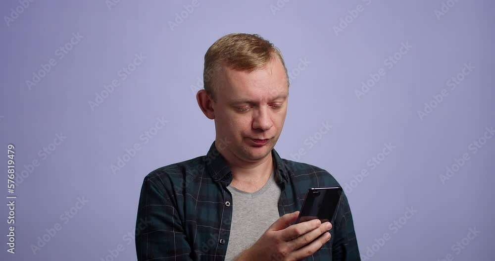 Young bored man is using smartphone standing in studio Young bored man is using smartphone standing in studio