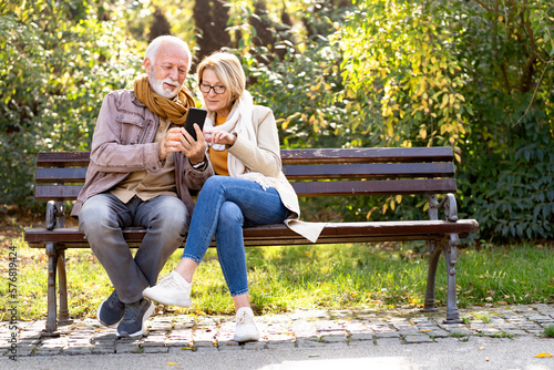 Cheerful elderly couple using banking apps on a smartphone to make payments outdoors in the park