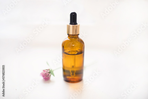Cosmetic bottle made of dark glass with a dispenser on a white background with fresh clover. Production of essential oil for cosmetology