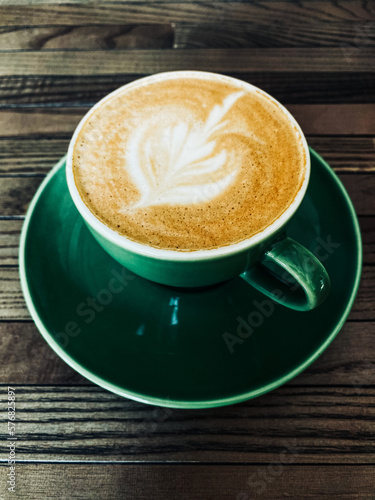 Cappuccino in a green cup on brown wooden textured table flat lay