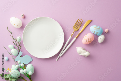 Easter decorations concept. Top view photo of empty plate cutlery fork knife floral decor pink white and blue eggs and ceramic bunny on isolated lilac background with blank space