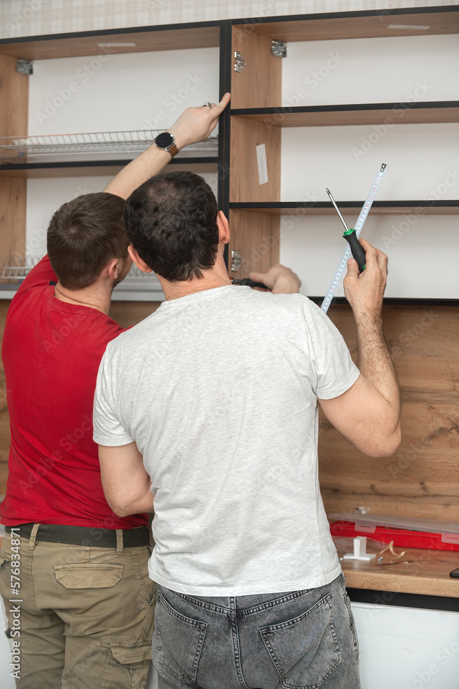 Two craftsmen, furniture makers and assemblers, are installing a modern kitchen in a home, tools in their hands. Concept furniture to order, improvement of living conditions, repair Two craftsmen, furniture makers and assemblers, are installing a modern kitchen in a home, tools in their hands. Concept furniture to order, improvement of living conditions, repair