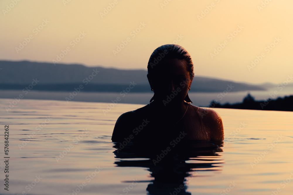 Fototapeta premium Girl at sunset in the pool. In the background, the sea and mountains.