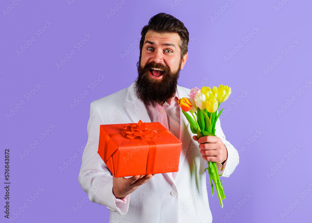 Smiling bearded man with gift box and bouquet of flowers. Businessman in suit with gift and bouquet of tulips. Romantic man with bouquet of flowers and present box. Valentines or Womens Day, birthday. Smiling bearded man with gift box and bouquet of flowers. Businessman in suit with gift and bouquet of tulips. Romantic man with bouquet of flowers and present box. Valentines or Womens Day, birthday.
