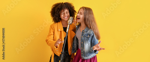 Teenage girls singing in microphone against yellow background