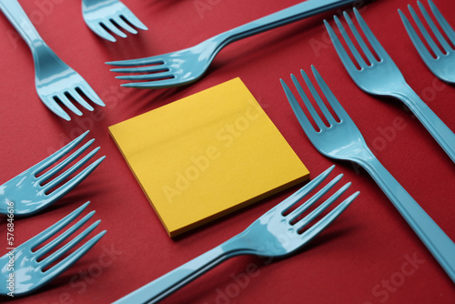 Group of blue forks on red background with blank adhesive note paper