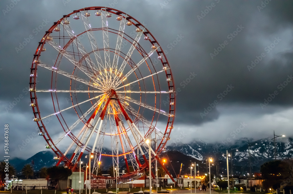 Ferris wheel in the evening, attraction, cloudy weather, clouds and mountains on the background