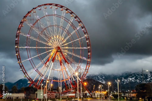 Ferris wheel in the evening, attraction, cloudy weather, clouds and mountains on the background