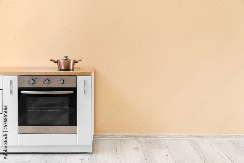 Fototapeta premium Pot on electric stove and oven near beige wall in kitchen