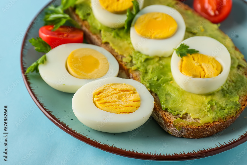 Plate with delicious avocado toast, boiled eggs and tomatoes on blue background Plate with delicious avocado toast, boiled eggs and tomatoes on blue background