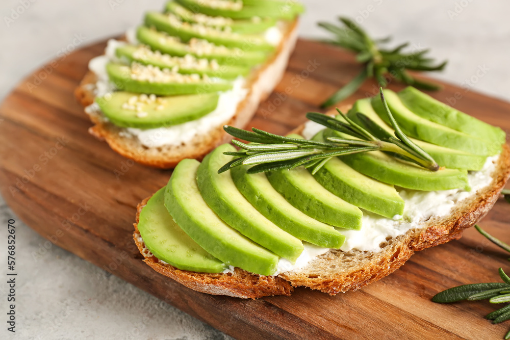Board with delicious avocado toasts and rosemary on grey background Board with delicious avocado toasts and rosemary on grey background