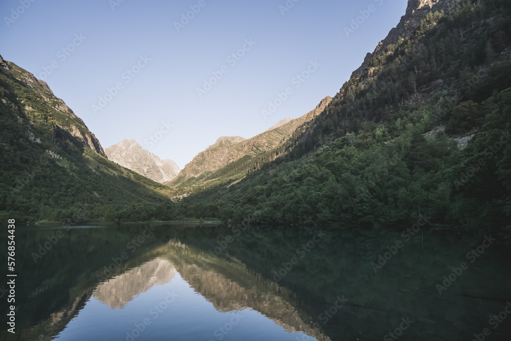 Morning landscape in the mountains with a lake in a valley between mountain slopes and rocks with a forest, a mirror surface of a mountain lake in the morning