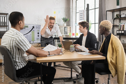 Group of four male multiracial business people in formal clothes having meeting with modern gadgets and documents at boardroom. Concept of teamwork and cooperation.