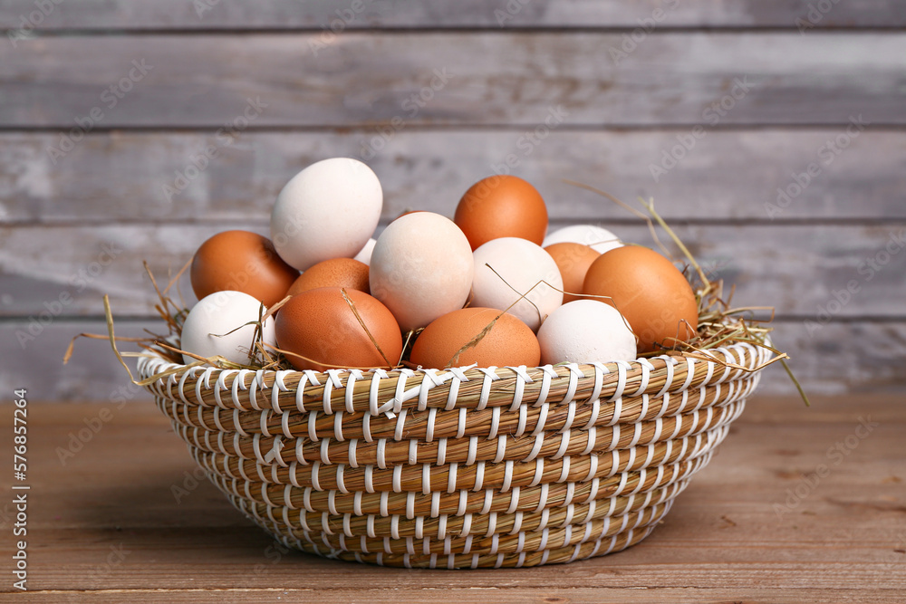 Wicker basket with Easter eggs and hay on wooden table near grey wall Wicker basket with Easter eggs and hay on wooden table near grey wall