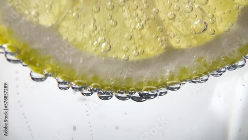 Slow Motion Macro shot of a lemon slice in water bubbles, Soft Drink with Ice, Bubbles, Mint and Lemon. Close Up Refreshment sparkles lemon soda and Cold Summer Drink.
