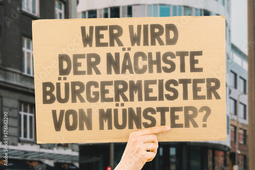 The phrase " Who's the next mayor of Münster? " on a banner in men's hands blurred the background. Election. City management. Politics. Urban. Voter. Candidate