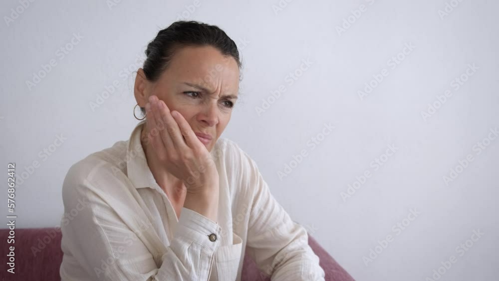 Female with gums disease indoor. A view of upset woman with gums pain sits on the sofa in the room. Female with gums disease indoor. A view of upset woman with gums pain sits on the sofa in the room.