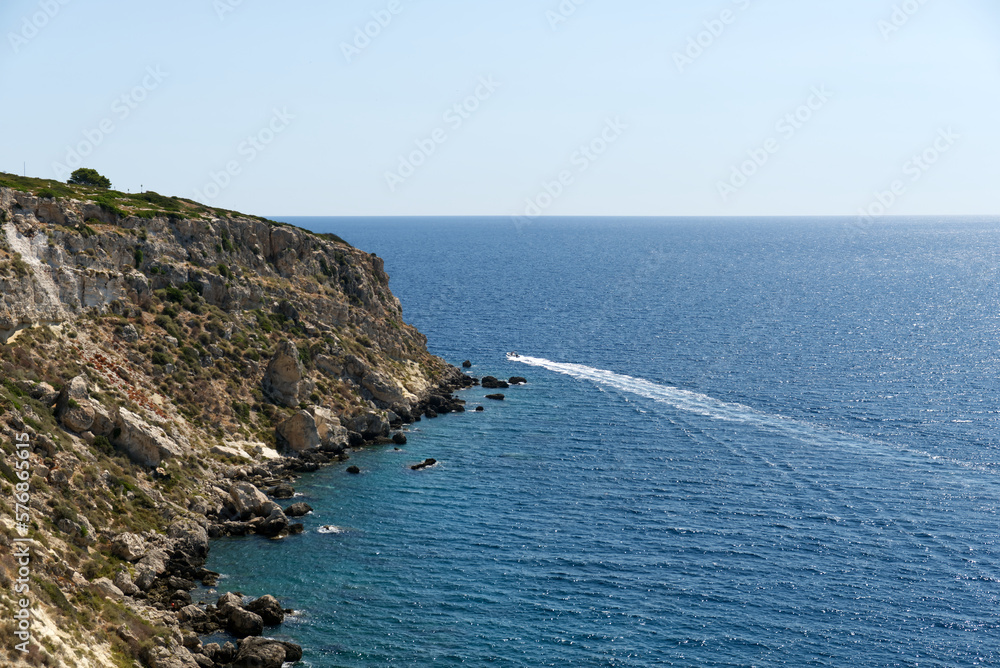 a boat goes around a rocky coast in a crystalline sea