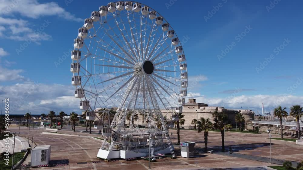 Panoramic view of the city of Civitavecchia with the adjoining tourist port and Forte Michelangelo. Emerald sea and view with tropical palm trees. Ferris wheel and cloudy sky. Panoramic view of the city of Civitavecchia with the adjoining tourist port and Forte Michelangelo. Emerald sea and view with tropical palm trees. Ferris wheel and cloudy sky.