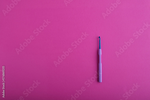 Fényképezés A blue shiny crochet hook with a light purple plastic handle is positioned as the main object against a large bright pink textured background