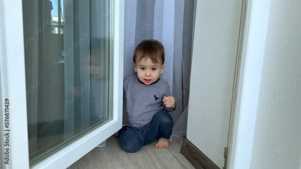 Beautiful kid playing in the balcony at home. Adorable toddler boy closes the glass door on the balcony. Beautiful kid playing in the balcony at home. Adorable toddler boy closes the glass door on the balcony.